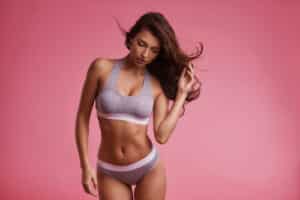 Attractive young woman in underwear posing while standing against pink background